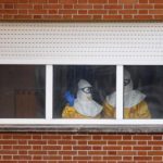 Health workers in protective suits stand at a window in the isolation ward of the Carlos III hospital in Madrid
