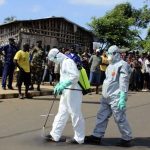 Health workers spray themselves with chlorine disinfectants after removing the body a woman who died of Ebola virus in the Aberdeen district of Freetown