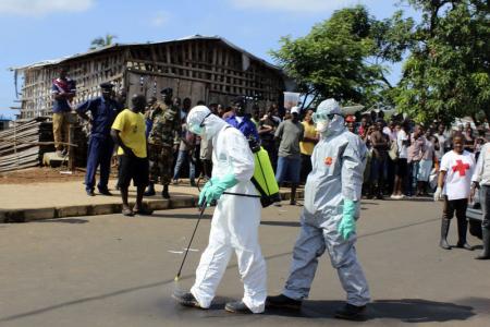 Health workers spray themselves with chlorine disinfectants after removing the body a woman who died of Ebola virus in the Aberdeen district of Freetown