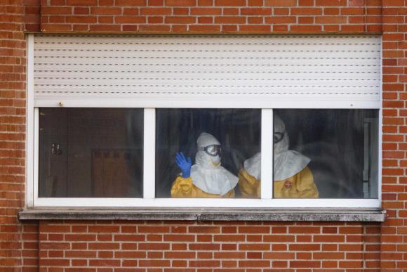 Health workers in protective suits stand at a window in the isolation ward of the Carlos III hospital in Madrid