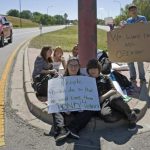 Protestors at Bear Creek High School sit on a street with their signs near the school in Lakewood, Colorado
