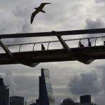 Workers cross the Millenium Bridge with the City of London seen behind, in London