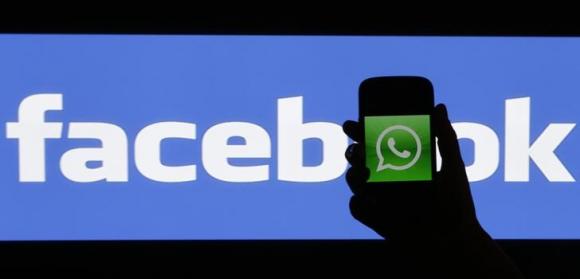 Woman holds a smartphone displaying WhatsApp's logo in front of the screen with the Facebook logo in this photo illustration taken in Prague