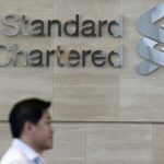 An office worker walks past a Standard Chartered logo outside its head office in Singapore