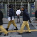 File photo of a man looking at a stock quotation board as passers-by walk past outside a brokerage in Tokyo
