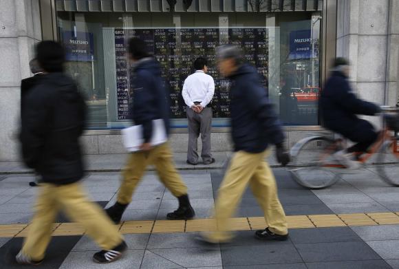 File photo of a man looking at a stock quotation board as passers-by walk past outside a brokerage in Tokyo