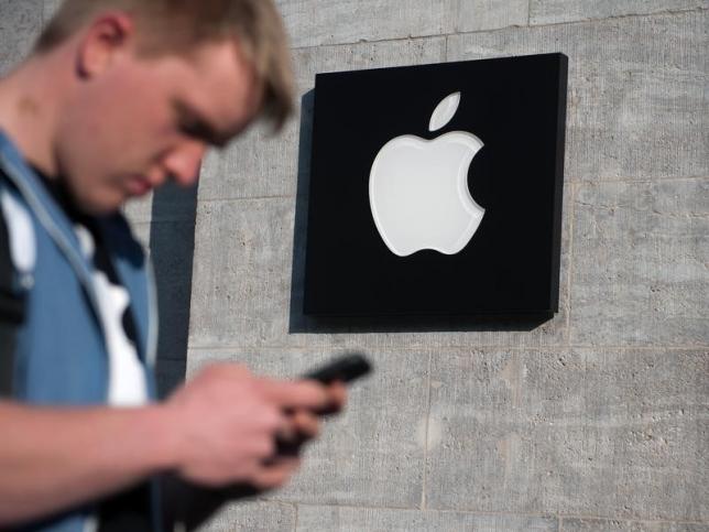An Apple logo is seen in front of an Apple Store as a customer waits to enter, in Berlin