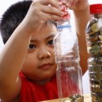 Little Boy Putting Money In A Bottle
