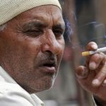 A man smokes a cigarette as he sits on a pavement along a road in Srinagar
