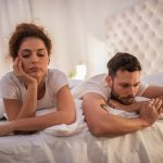 Young couple lying in bed while having problems in their relationship.