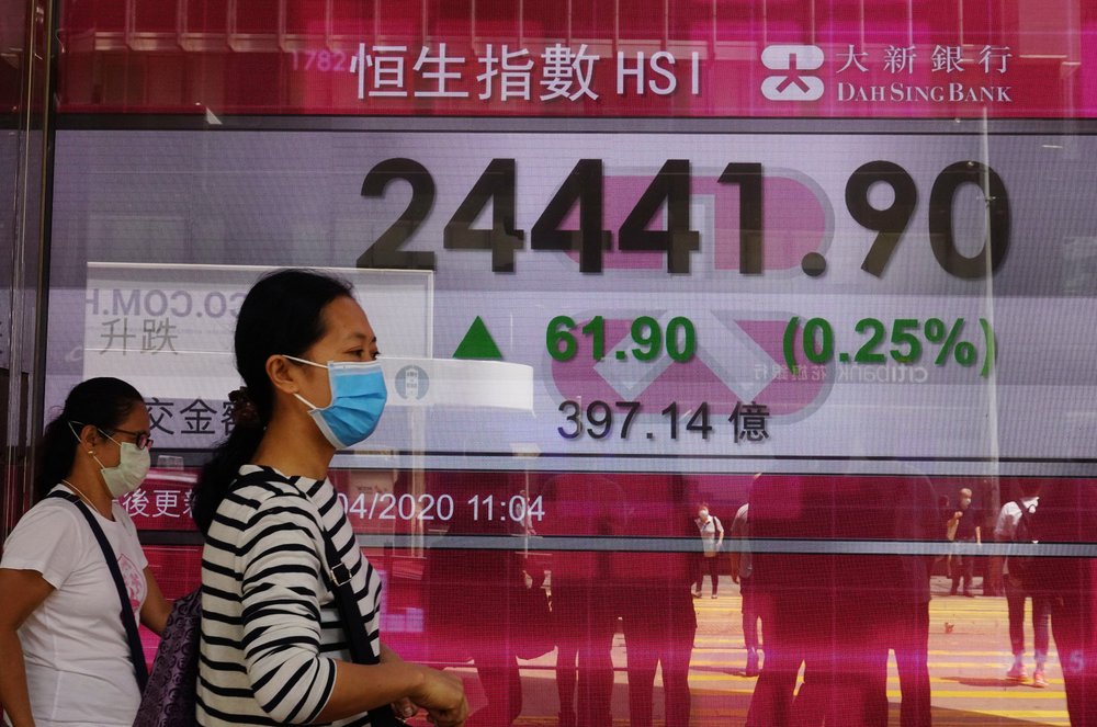 People wearing face masks walk past a bank electronic board showing the Hong Kong 