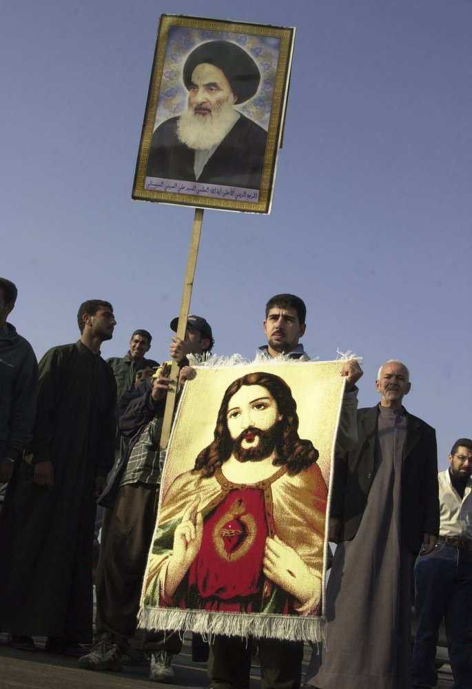 An Iraqi Christian holds a carpet with an image of Jesus Christ and a poster of Grand Ayatollah Ali al-Husseini al-Sistani during a march in Baghdad