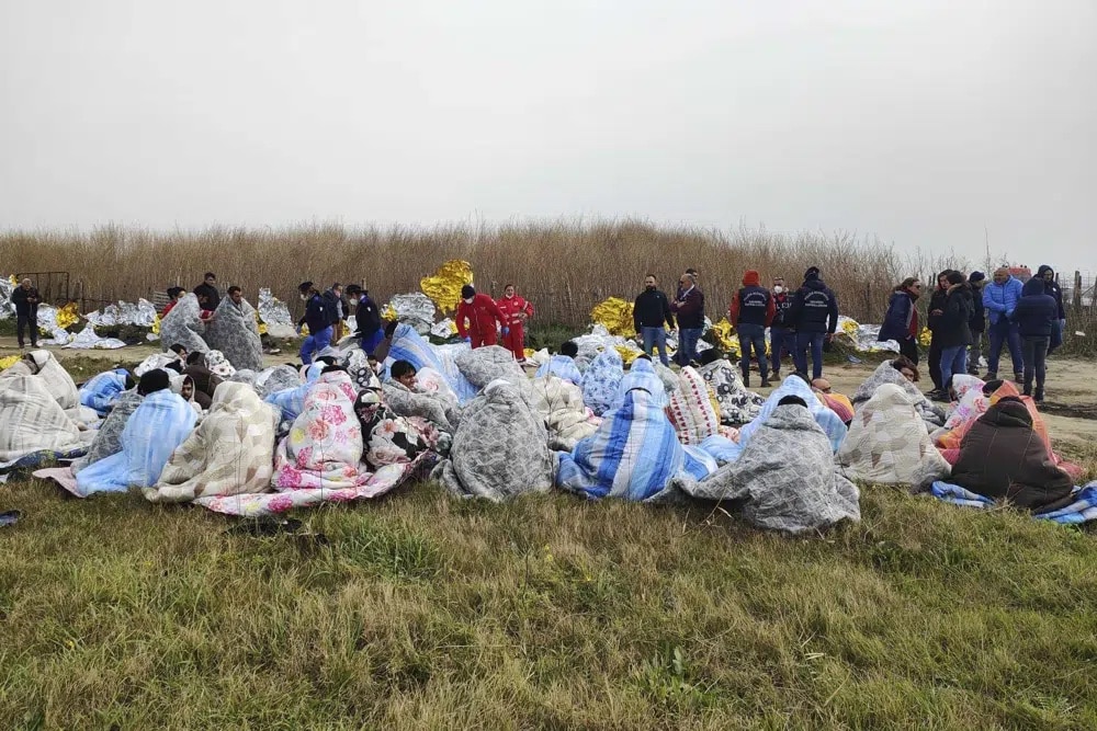 Rescued migrants sit covered in blankets at a beach near Cutro, southern Italy. 