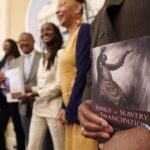 Dr. Amos C. Brown, Jr., vice chair for the California Reparations Task Force, right, holds a copy of the book Songs of Slavery and Emancipation, as he and other members of the task force pose for photos at the Capitol in Sacramento, Calif