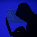 A hooded man holds a laptop computer as blue screen with an exclamation mark is projected on him in this illustration picture taken on May 13, 2017.