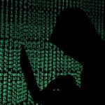 A hooded man holds a laptop computer as cyber code is projected on him in this illustration picture taken on May 13, 2017.