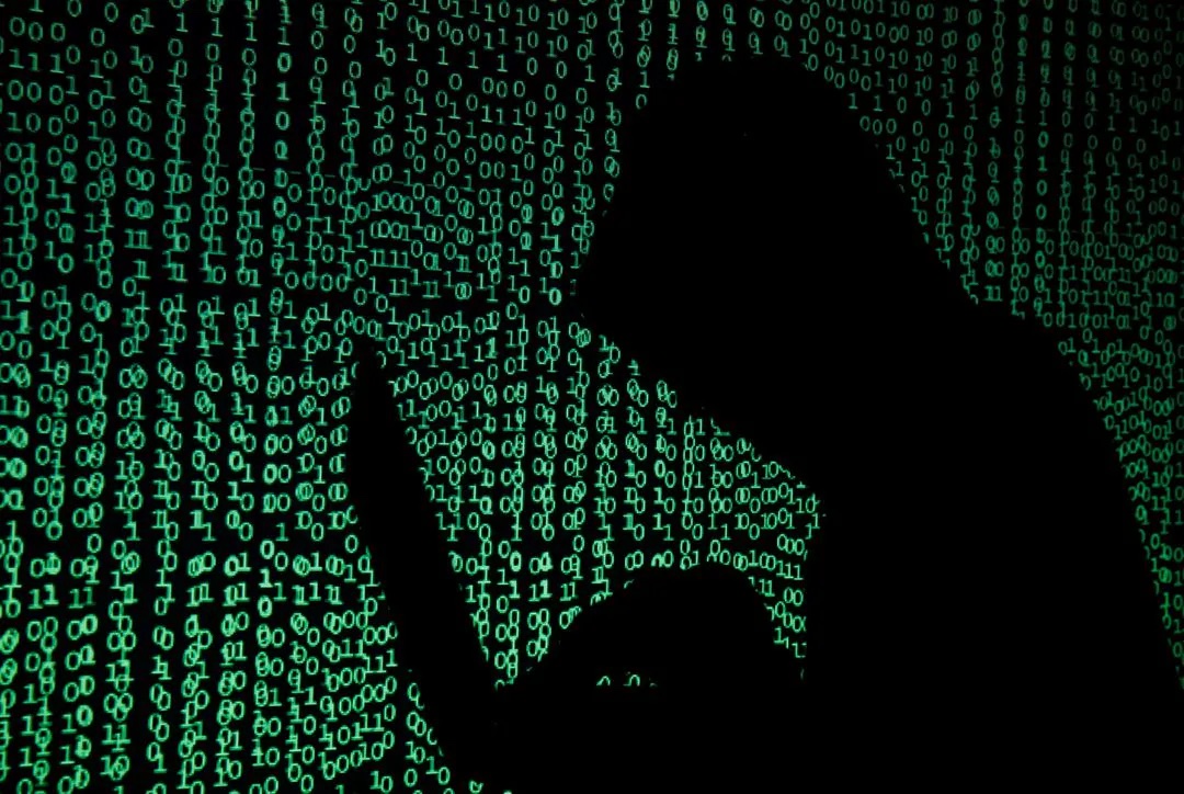 A hooded man holds a laptop computer as cyber code is projected on him in this illustration picture taken on May 13, 2017. 