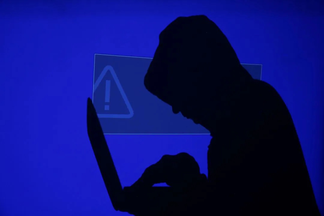 A hooded man holds a laptop computer as blue screen with an exclamation mark is projected on him in this illustration picture taken on May 13, 2017.