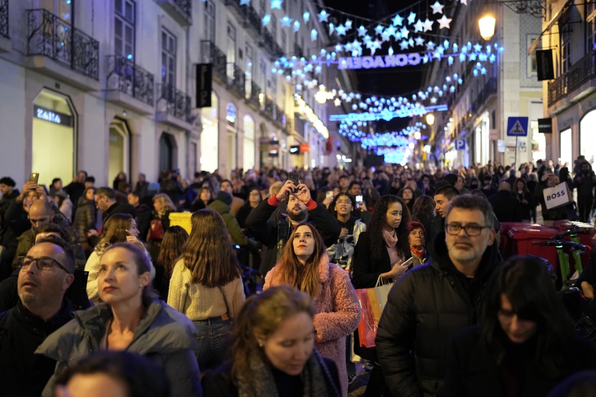 eople look up at Christmas lights as crowds stroll around downtown Lisbon’s Chiado neighborhood, Saturday evening, Dec. 23, 2023. (AP Photo/Armando Franca)