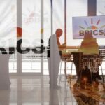Delegates interact next to the logos of the BRICS summit during the 2023 BRICS Summit at the Sandton Convention Centre in Johannesburg, South Africa on August 23, 2023.