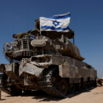 Israeli soldiers mount an Israeli flag on a military vehicle near the Israel-Gaza border