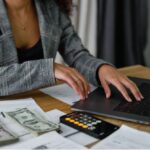 A woman using a laptop near cash money