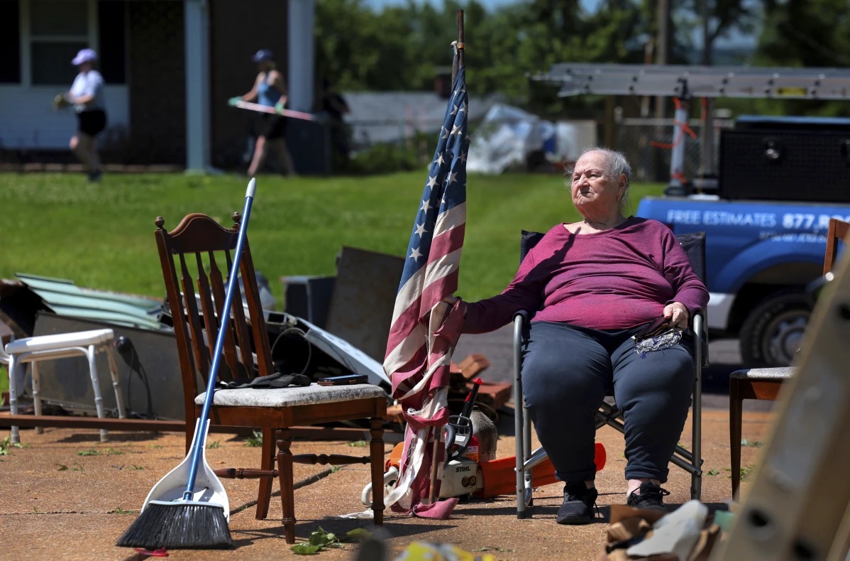 Jackie Moloney, 88, hangs on to her shredded American flag on Monday, May 27, 2024 as her family cleans up on Morningdale Place in Mehlville, Mo. 