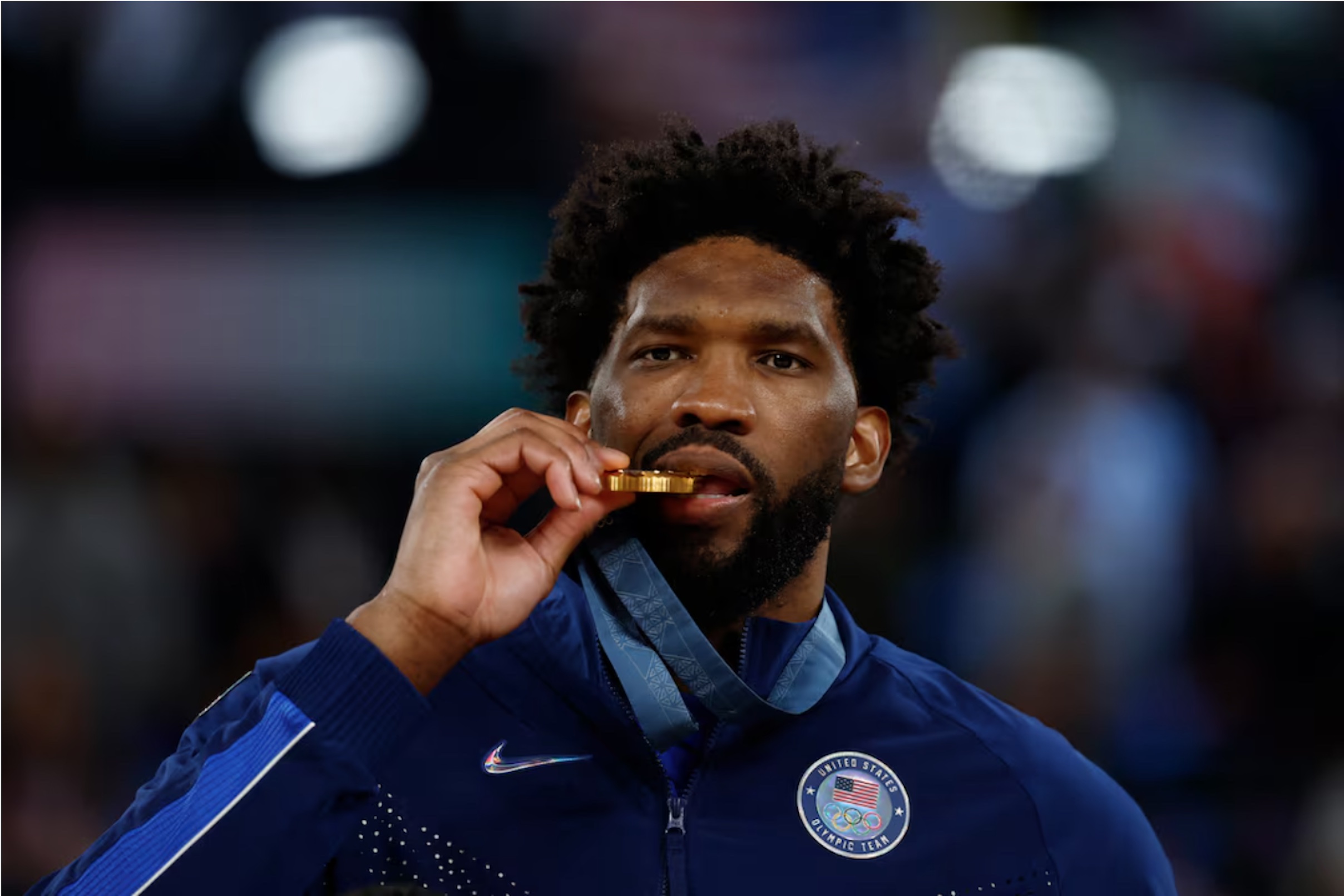 Paris 2024 Olympics - Basketball - Men's Victory Ceremony - Bercy Arena, Paris, France - August 10, 2024. Gold medallist Joel Embiid of United States bites his medal.