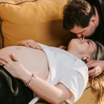Pregnant woman lying on couch has a romantic moment with her man