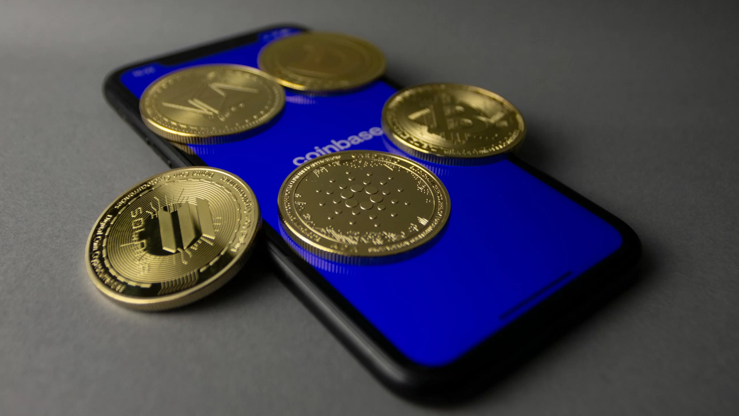 Studio shot of gold coins lying on top of a smartphone displaying coinbase app.