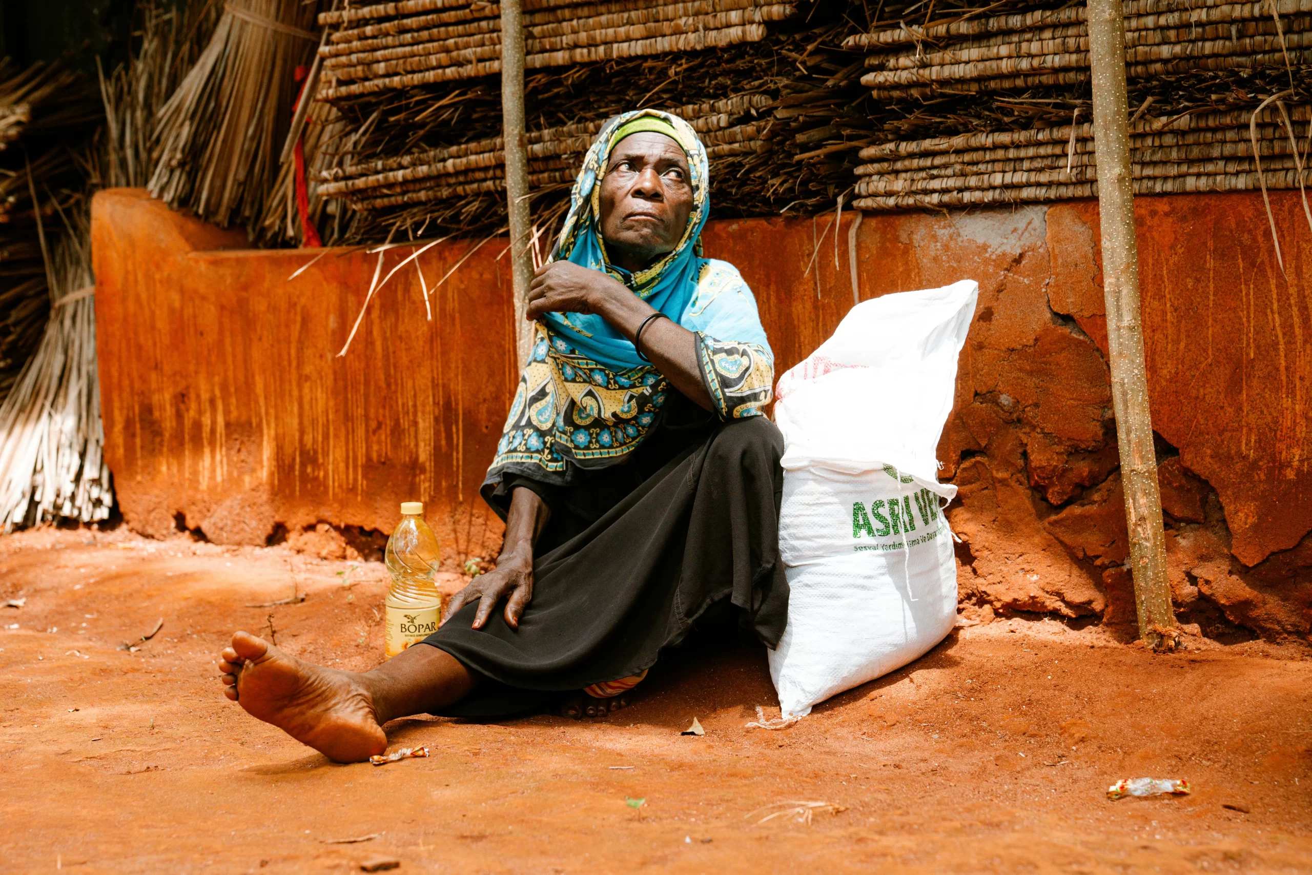 Elderly woman sitting on red earth in village (illustration image).