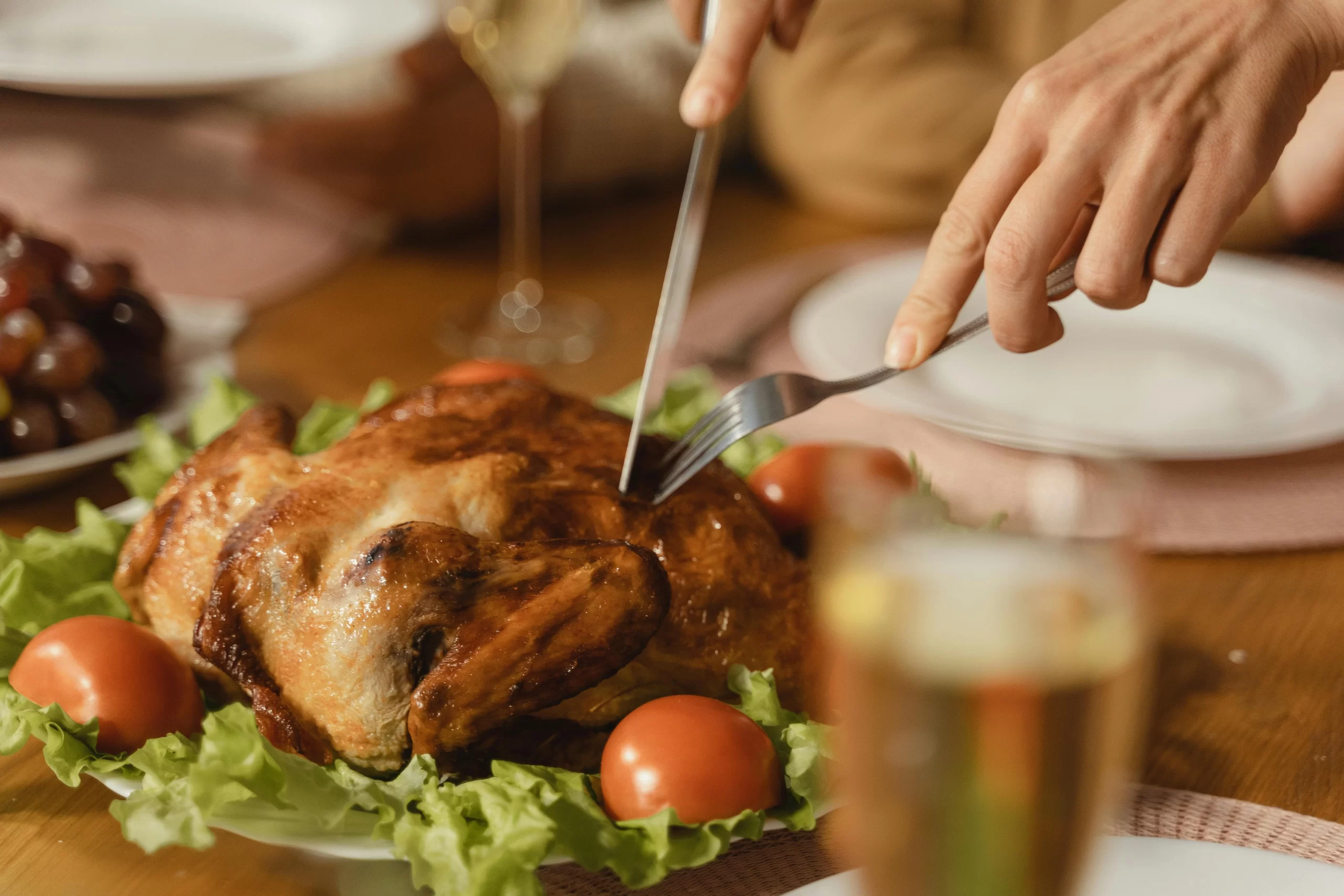 A person holding fork and knife slicing cooked turkey meat.
