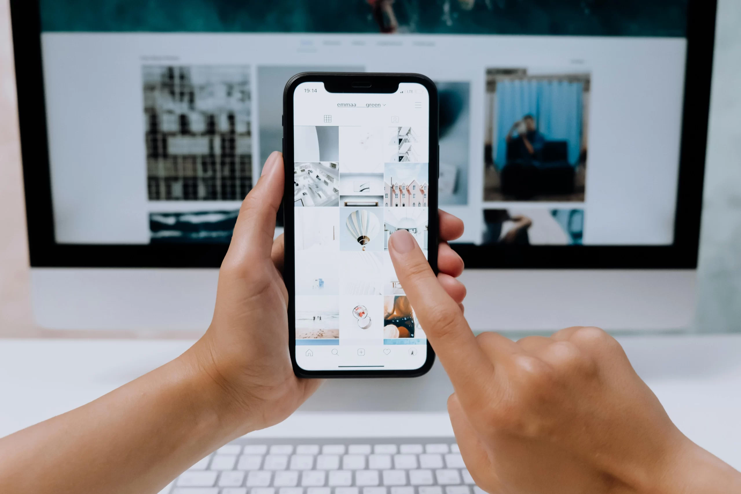 A person in front of computer checking image through a smartphone.