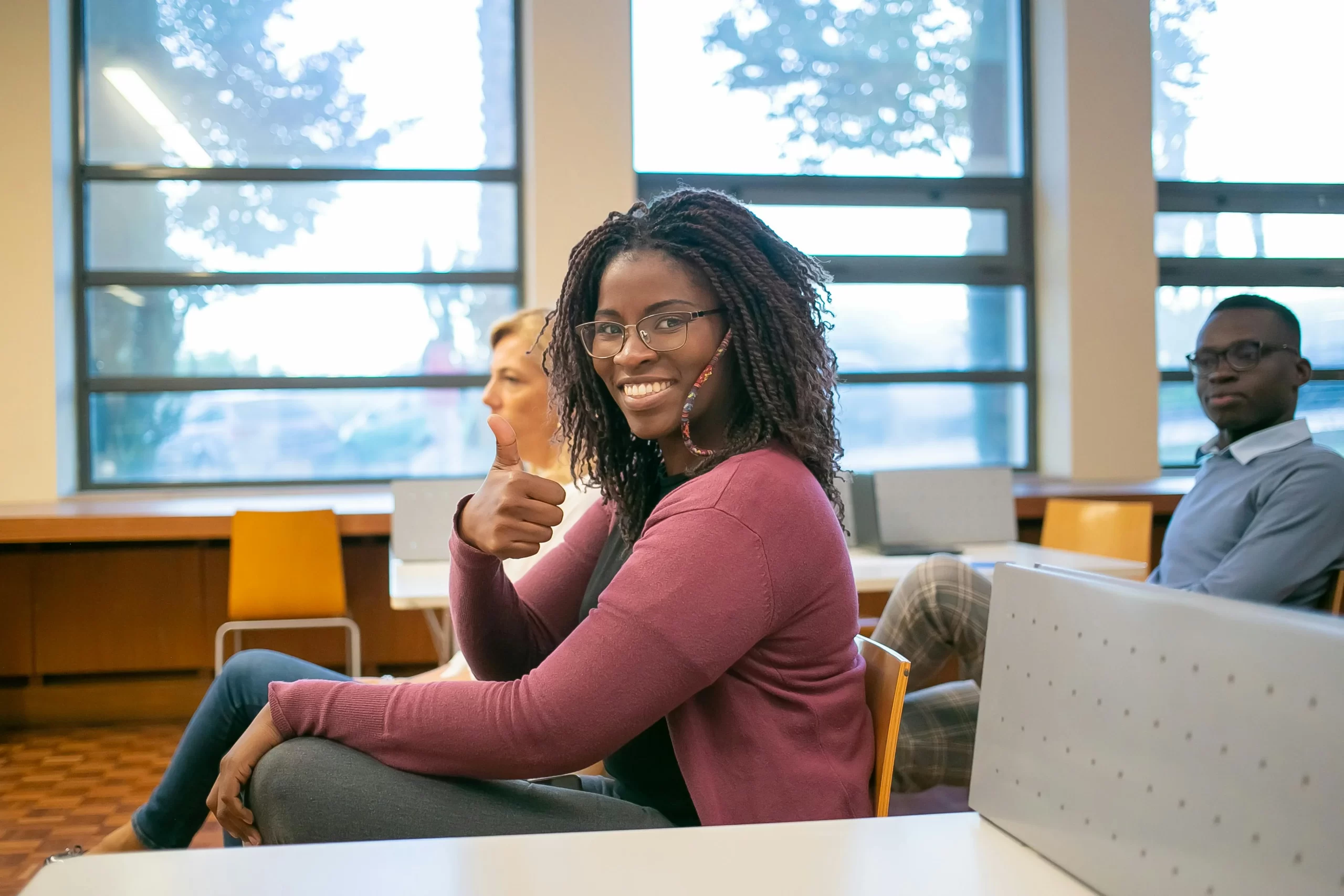 Student woman in a classroom showing thumb up to camera.