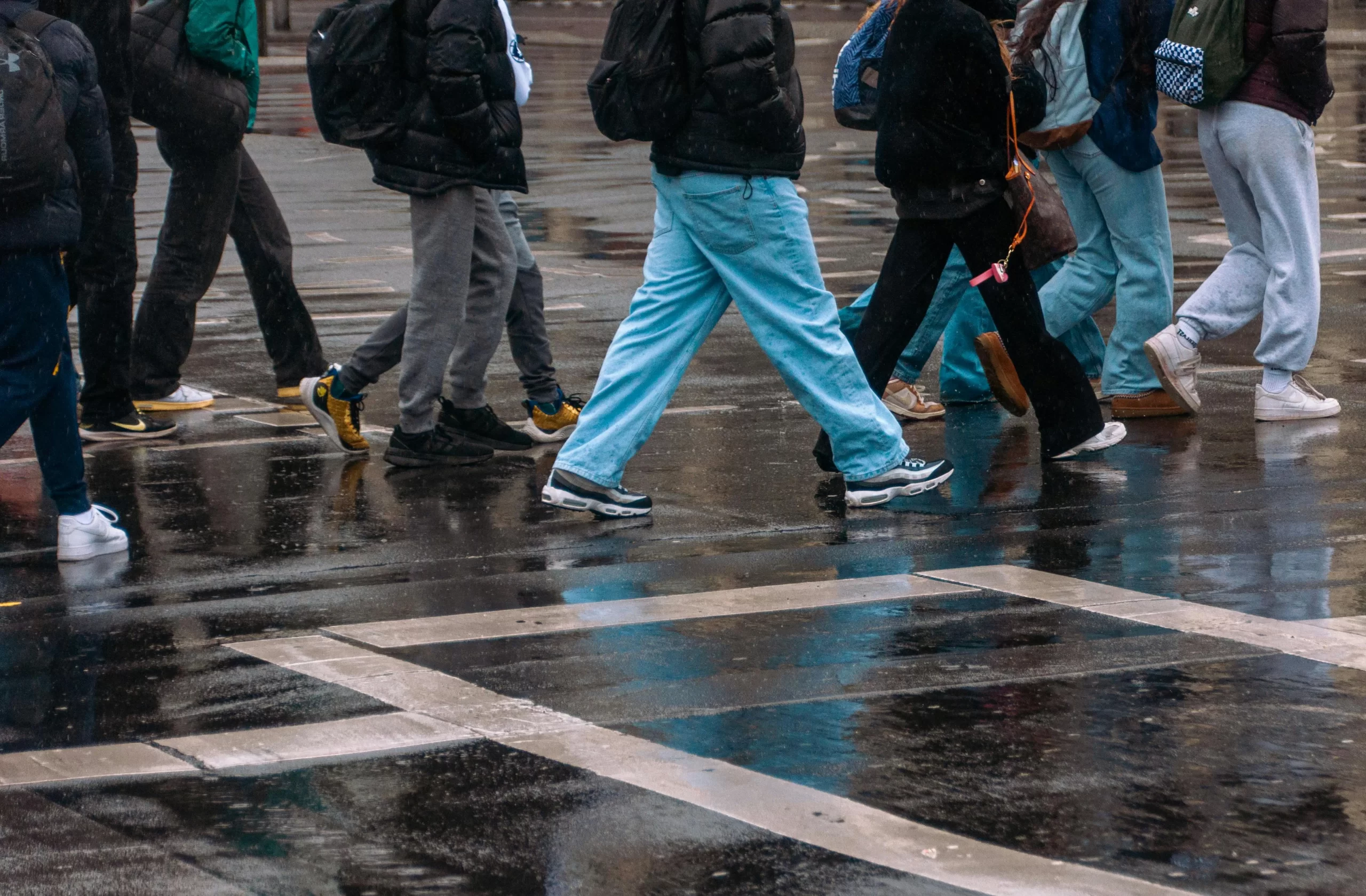People crossing a wet city street in rainy weather.
