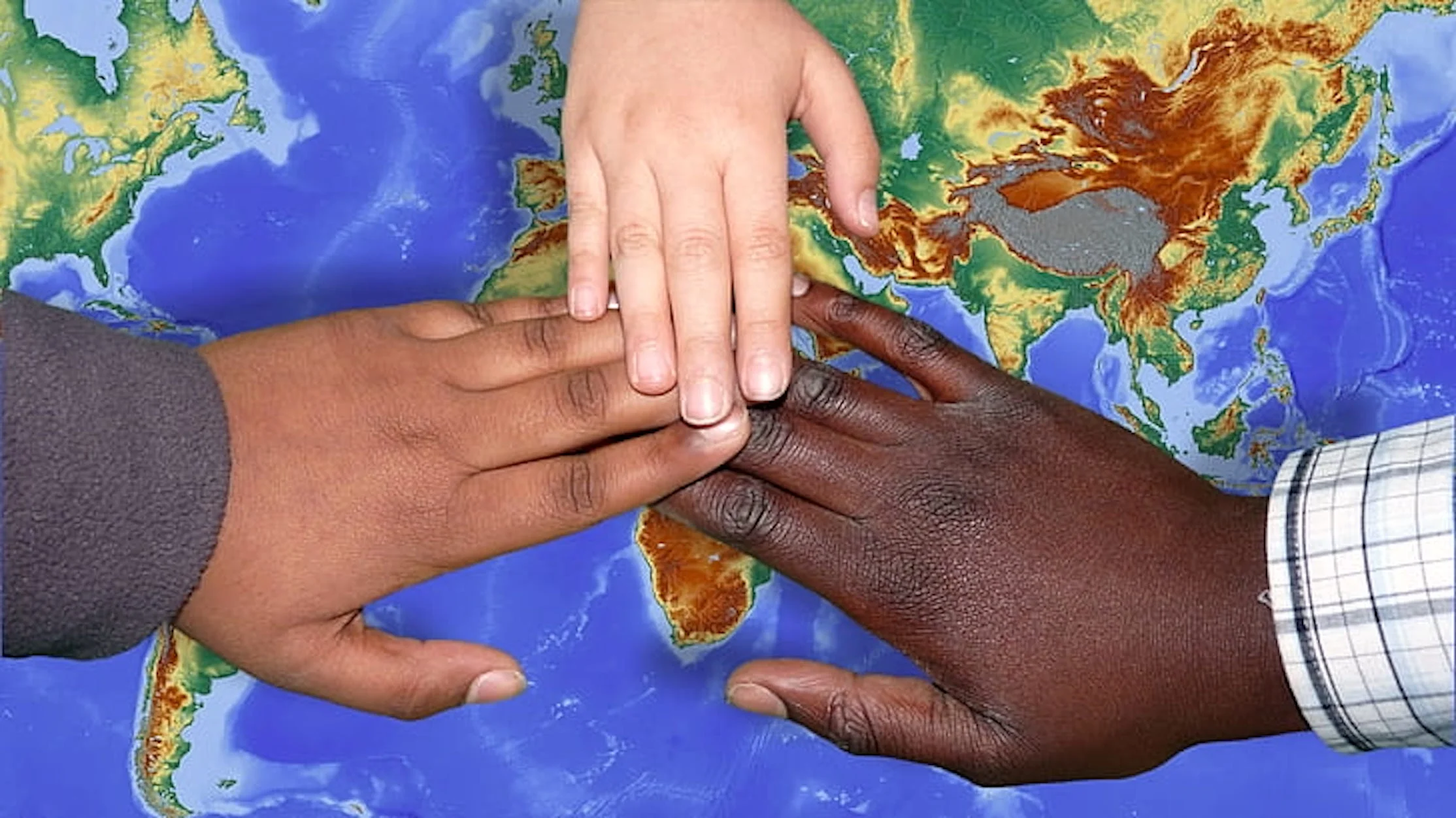 Hands of three people on top of World map.