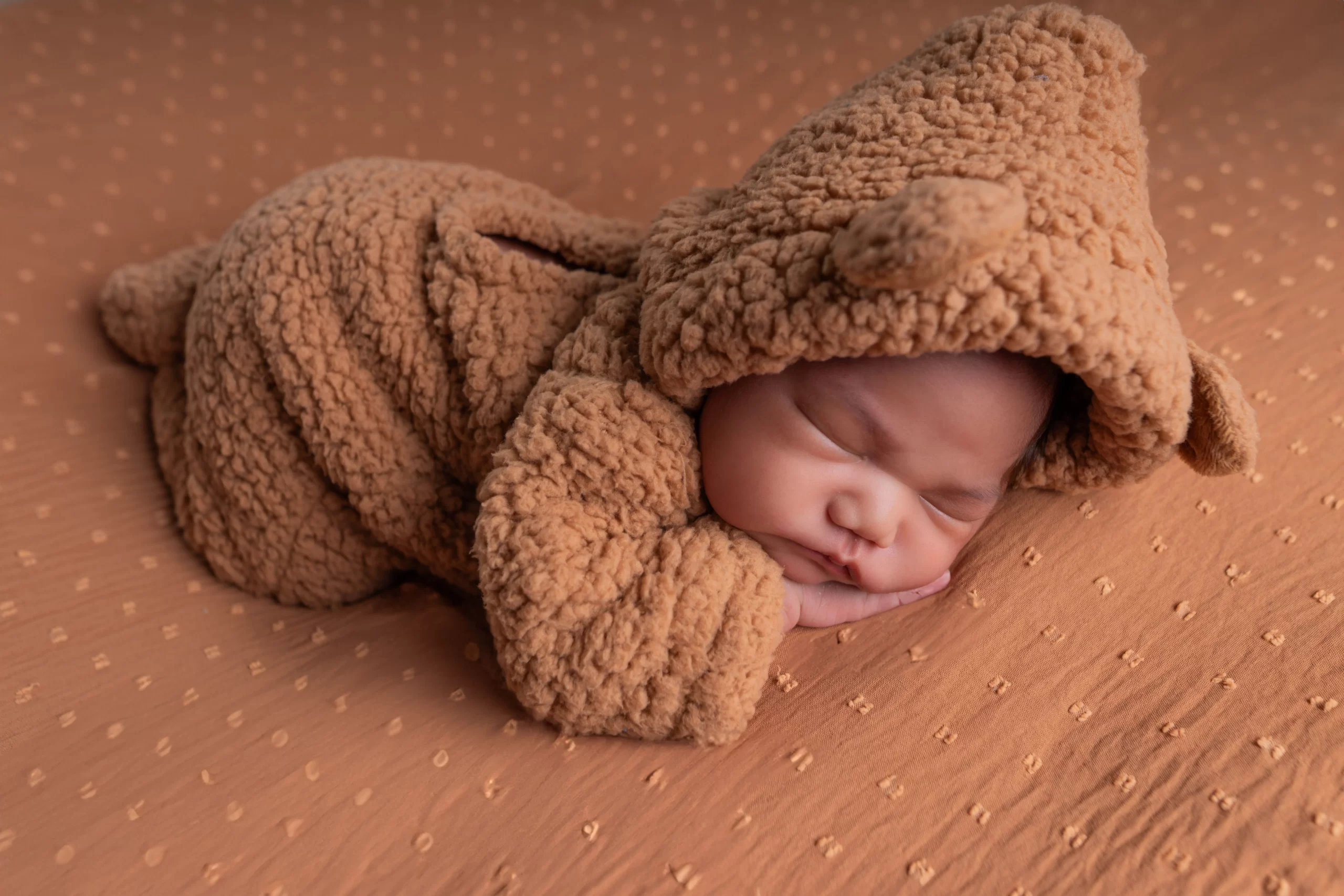 A cute newborn baby peacefully sleeping in a soft, brown bear costume.