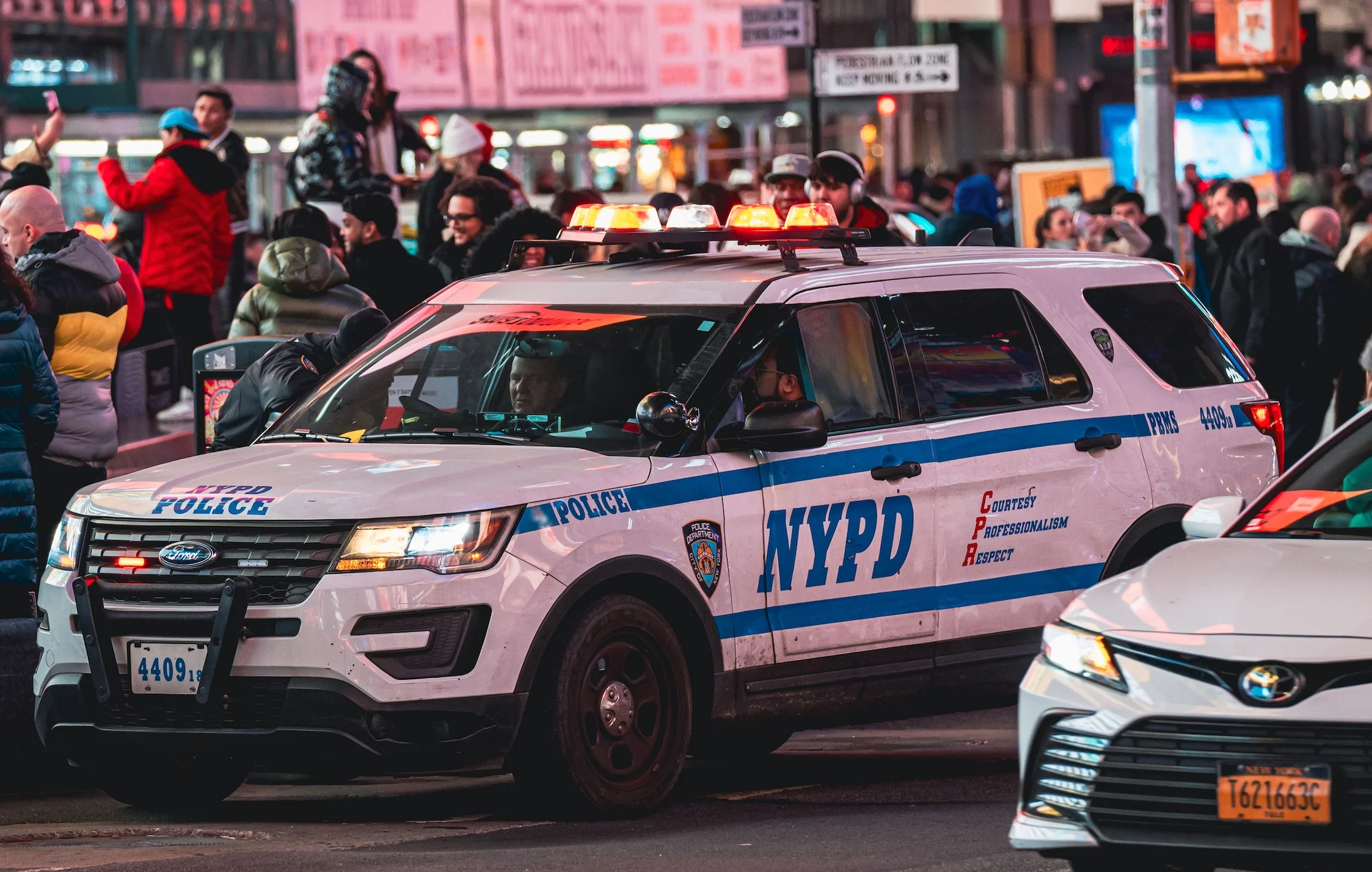 NYPD vehicle patrolling a busy city street in New York at night.