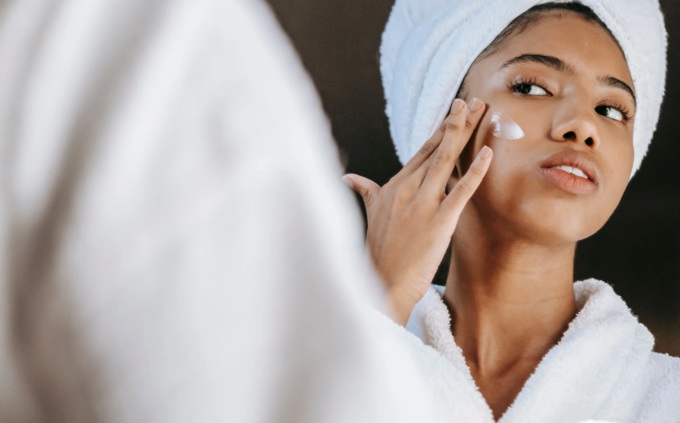 A Woman in a bathrobe practices her skincare routine with moisturizing cream.