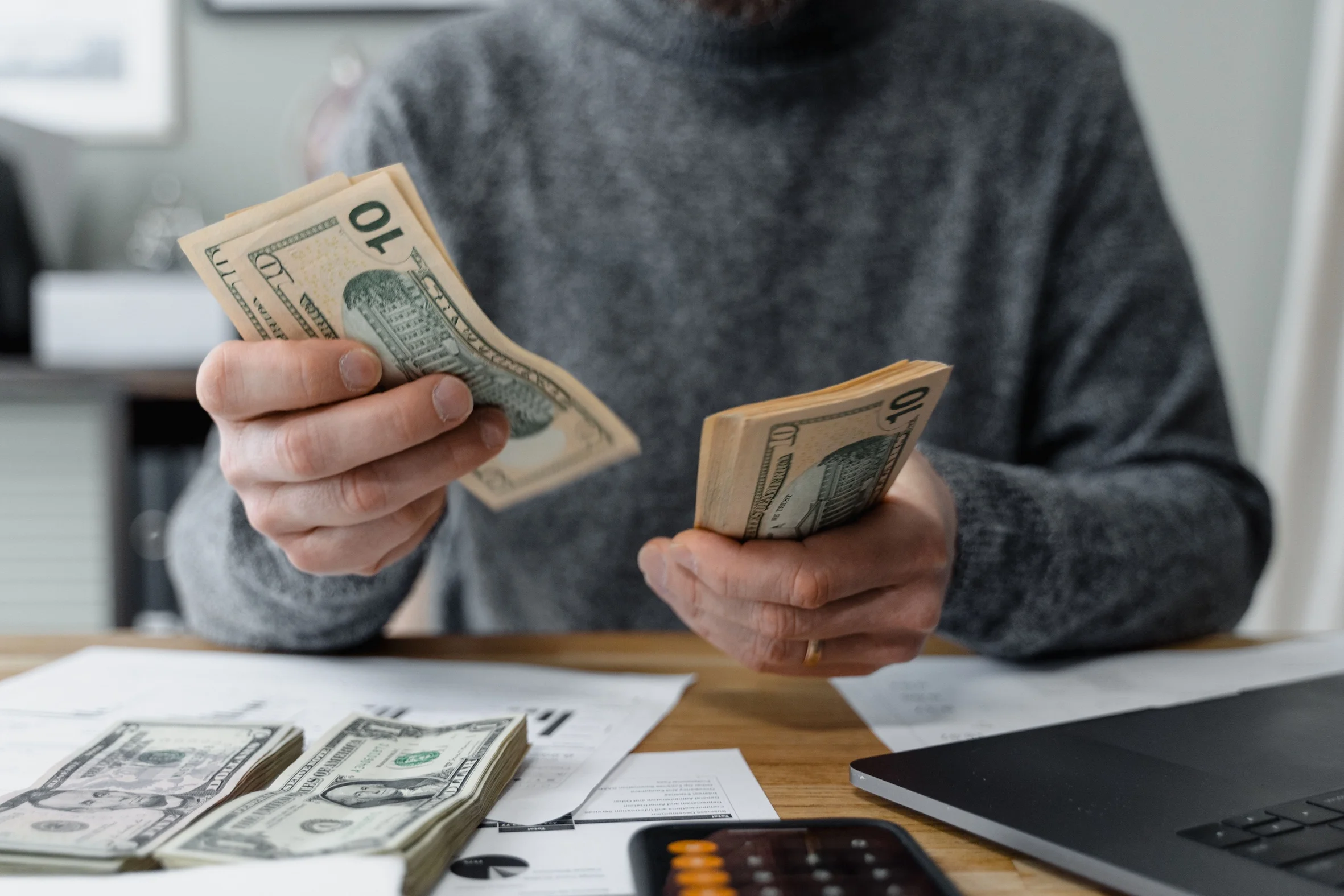 A person counting cash with a calculator and paperwork on a desk.