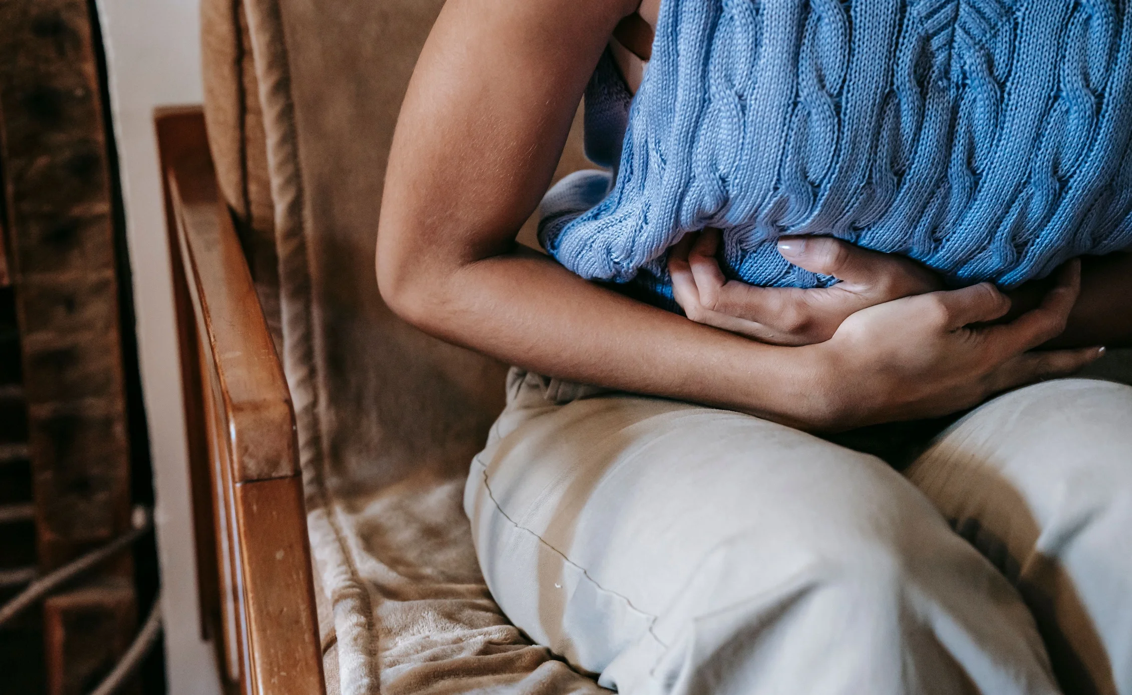A woman holding a pillow against her stomach, indicating discomfort or pain.